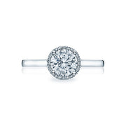 A slim bloom of diamonds encircles a round center diamond for an elegant and modern solitaire with a dainty modern crescent silhouette profile. The diamonds culet is just visible kissing a sweetheart carriage for an elegantly modern and sophisticated look.