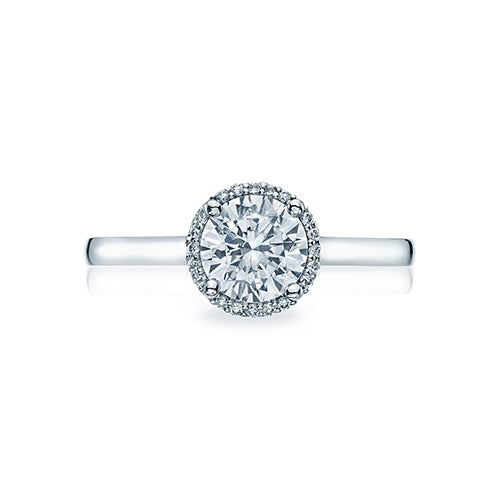 A slim bloom of diamonds encircles a round center diamond for an elegant and modern solitaire with a dainty modern crescent silhouette profile. The diamonds culet is just visible kissing a sweetheart carriage for an elegantly modern and sophisticated look.