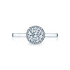 A slim bloom of diamonds encircles a round center diamond for an elegant and modern solitaire with a dainty modern crescent silhouette profile. The diamonds culet is just visible kissing a sweetheart carriage for an elegantly modern and sophisticated look.